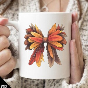 May include: White ceramic mug with a colorful illustration of a bow made of feathers. The feathers are in shades of orange, brown, and yellow.