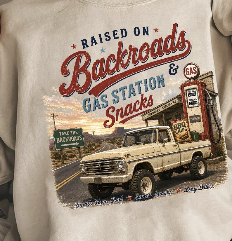 May include: Cream-colored sweatshirt with a graphic featuring a vintage pickup truck, gas station, and the text "RAISED ON Backroads & GAS STATION Snacks." The design includes a road sign that says "TAKE THE BACKROADS."