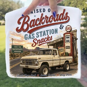 May include: White t-shirt featuring a vintage design with the words "Raised on Backroads Gas Station Snacks." The graphic includes a classic pickup truck, gas pump, and a desert road scene. The shirt also has the text "Take the Backroads."