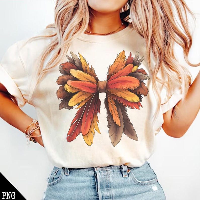 May include: A white t-shirt with a large, colorful bow made of feathers. The bow is made of orange, red, brown, and yellow feathers.