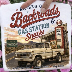 May include: White t-shirt with a vintage graphic of a beige pickup truck at a gas station, with the text "RAISED ON Backroads GAS STATION Snacks". Includes a sign that says "TAKE THE BACKROADS". Also has the text "Small Town Soul Sweet Snacks Long Drives".