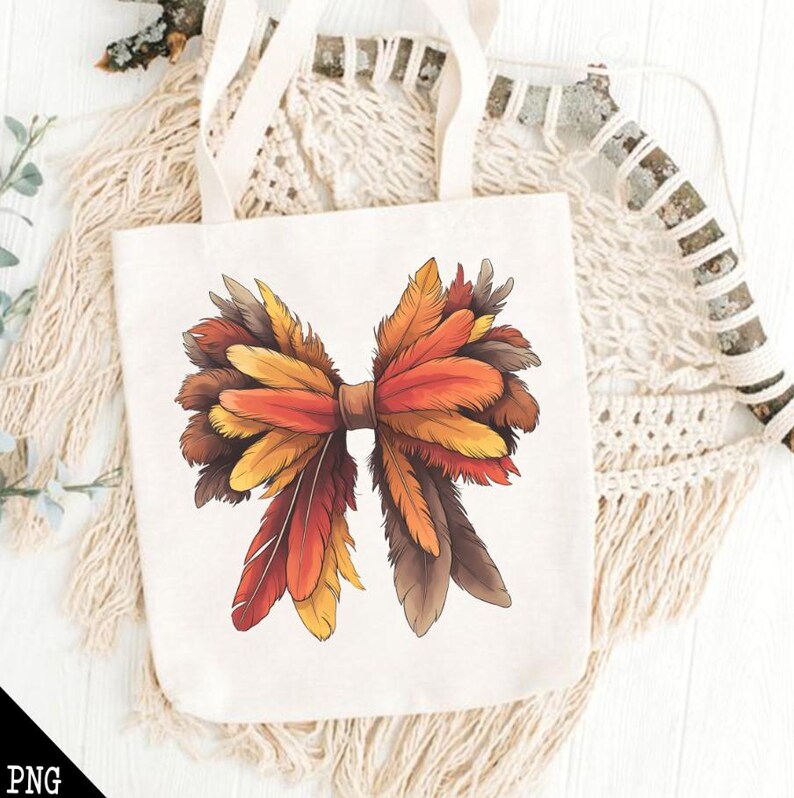 May include: A white tote bag with a brown, orange, and yellow feather bow design. The bag has two handles and is made of canvas.