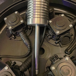 May include: A silver metal rod with a threaded end and a ribbed section. The rod is surrounded by black electrical components.