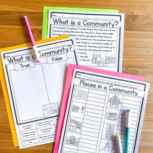 May include: Educational worksheets titled "What is a Community?" and "Places in a Community" are displayed. A pink marker rests on the "True" and "False" worksheet. The worksheets are on colored paper, with text and illustrations.
