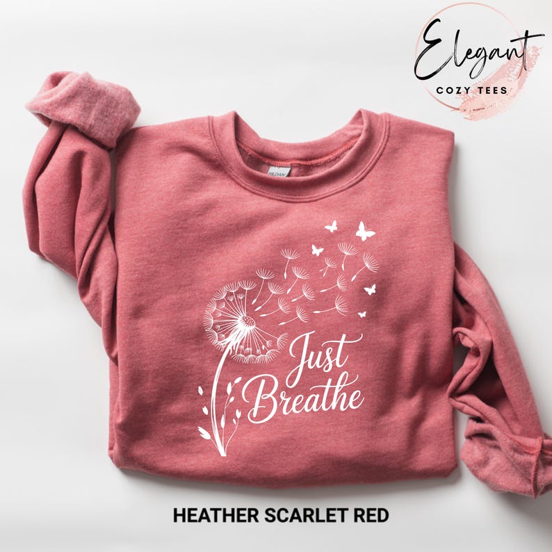 Peut inclure: Un sweat-shirt &agrave; manches longues rouge &eacute;carlate chin&eacute; avec un motif blanc repr&eacute;sentant un pissenlit dont les graines s'envolent et de petits papillons. Le texte Just Breathe est imprim&eacute; en &eacute;criture blanche sous le motif du pissenlit.