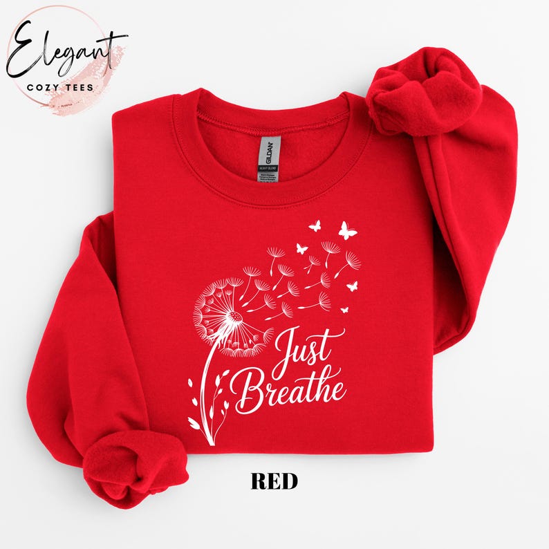 Peut inclure: Un sweat-shirt rouge vif &agrave; manches longues et col rond, orn&eacute; d'un motif blanc repr&eacute;sentant un pissenlit dont les graines se transforment en petits papillons. Le texte Just Breathe est imprim&eacute; en lettres cursives blanches.