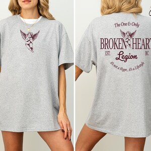 Grey t-shirt with cupid graphic and "Broken Heart Legion" text on back.