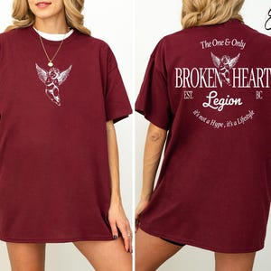 Burgundy t-shirt with angel graphic on front and "Broken Heart Legion" text on back.