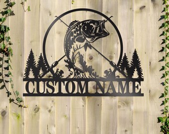 May include: Black metal wall art featuring a bass fish jumping out of the water with crossed fishing rods and a forest silhouette. The text "CUSTOM NAME" is displayed below the fish.