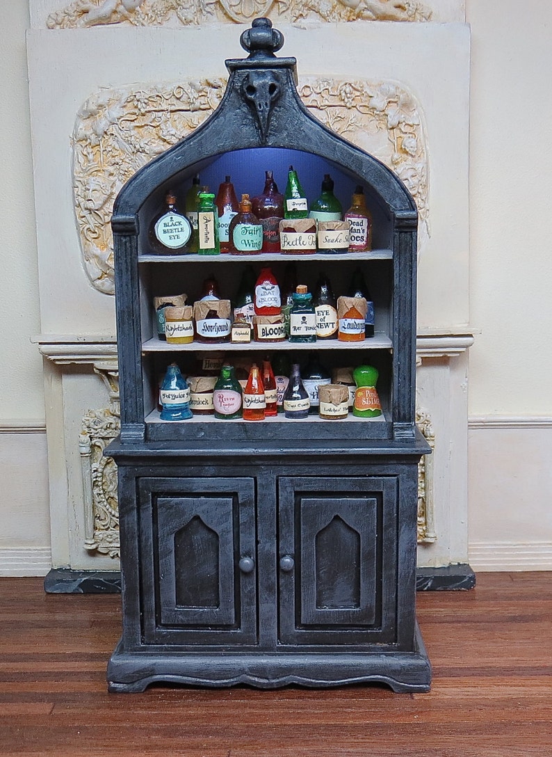 May include: A black wooden cabinet with glass doors and shelves filled with potion bottles. The bottles have labels with names like "Fairy Wine", "Beetle Juice", and "Blood".