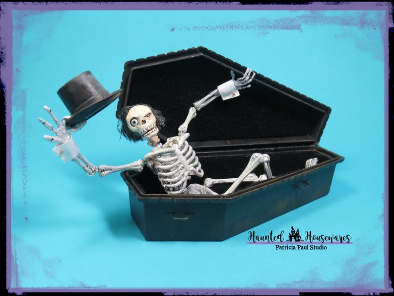 May include: A skeleton wearing a top hat and white cuffs is sitting up in a black coffin. The coffin is open and the skeleton is looking up. The background is a bright blue.
