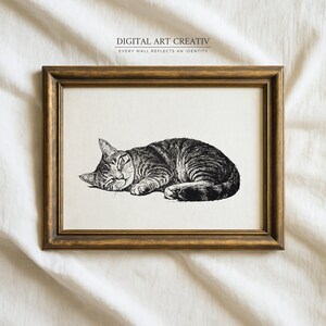 Pode incluir: Uma impress&atilde;o emoldurada com uma ilustra&ccedil;&atilde;o detalhada em preto e branco de um gato malhado dormindo. A obra de arte est&aacute; em um fundo creme e emoldurada em uma moldura de madeira dourada. O texto "DIGITAL ART CREATIV" e "EVERY WALL REFLECTS AN IDENTITY" &eacute; impresso no topo.