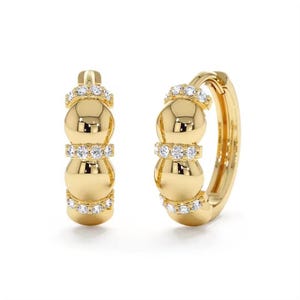 May include: A pair of gold-colored hoop earrings. Each earring features three rounded sections separated by a band of small, clear gemstones. The top and bottom of each earring also have a band of gemstones. The earrings are displayed against a white background.