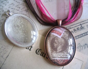 May include: Two oval pendants. One is a silver-toned setting with a textured interior. The other is a copper-toned pendant with a vintage stamp design under glass. The stamp features a profile and the text "3-CENTAVOS". Pink and brown ribbons are attached.