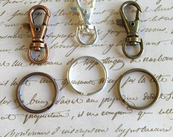 May include: Three silver and bronze keychains with a ring and a clasp. The keychains are on a white surface with handwritten text.