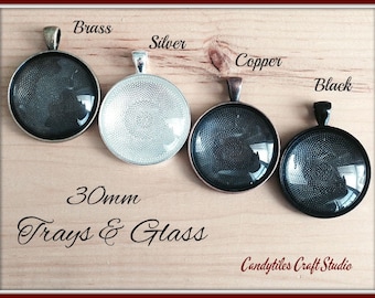 Op de afbeelding: Vier ronde glazen trays met metalen frames in messing, zilver, koper en zwart, elk 30 mm in diameter.