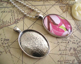 May include: Two silver oval pendant trays, one with a pink floral design and the other empty. The trays are on a map background.
