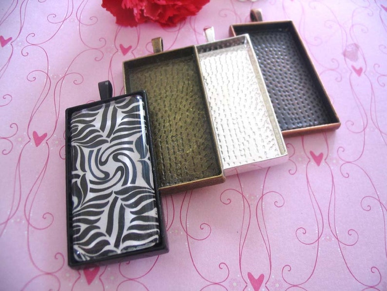 Puede incluir: Cuatro marcos rectangulares de metal con acabado plateado, cobre, negro y dorado. Los marcos est&aacute;n dise&ntilde;ados para contener un inserto de vidrio o pl&aacute;stico para la elaboraci&oacute;n de joyas.