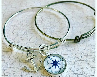 May include: Two silver bangle bracelets with charms. One charm is an anchor and the other is a compass with the words "A Life On The Sea" and "Liberty" around the compass.