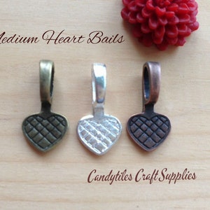 May include: Three heart-shaped metal bails in different finishes: antique brass, silver, and copper. Each bail has a textured surface and is designed for attaching to jewelry or crafts.