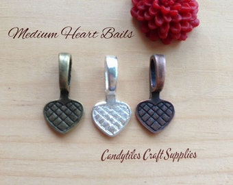 May include: Three heart-shaped metal bails in different finishes: antique brass, silver, and copper. Each bail has a textured surface and is designed for attaching to jewelry or crafts.