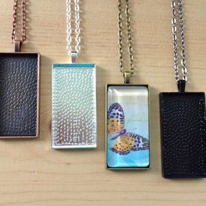 May include: Four silver, copper, and black pendant trays with chains. The trays are rectangular and have a textured surface. One tray has a glass insert with a butterfly image.