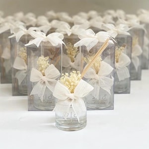 Può includere: Un gruppo di piccole bottiglie di vetro con fiori secchi e un bastoncino di legno all'interno. Ogni bottiglia è legata con un nastro bianco e ha un'etichetta personalizzata con la data "10.02.2024".