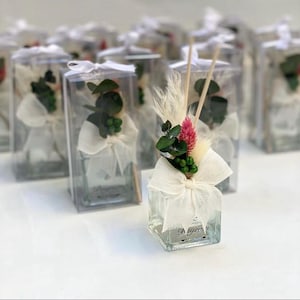 May include: A set of small glass bottles with white ribbon bows and dried flowers. The bottles contain a clear liquid and wooden sticks. The bottles are labelled with the text "Le yvon" and the date "07.10.2022".