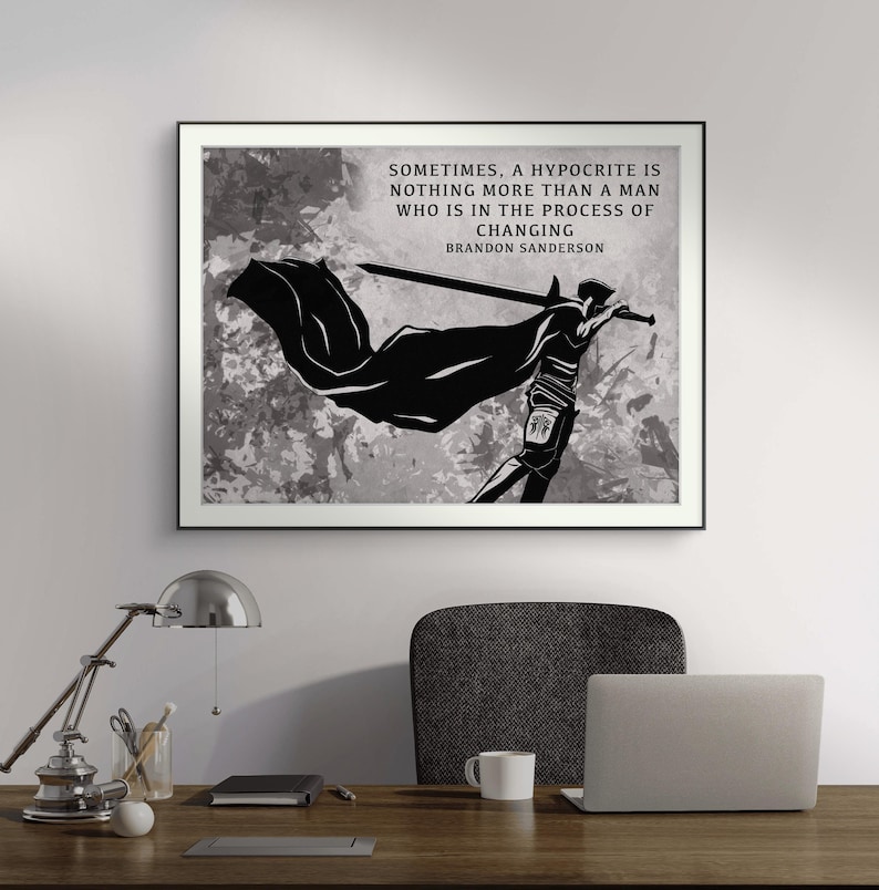 May include: A framed black and white art print with a silhouette of a figure holding a sword and cape. The print displays the quote "Sometimes, a hypocrite is nothing more than a man who is in the process of changing" by Brandon Sanderson.