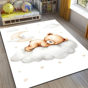 Può includere: Un tappeto rettangolare bianco con un design stravagante. Un orsacchiotto marrone chiaro dorme su una soffice nuvola bianca. Una luna crescente e stelle sono presenti. Il tappeto è per la cameretta di un bambino.