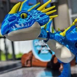 May include: A blue and yellow dragon figurine with a detailed, textured design. The dragon has a white underbelly and sharp teeth. The figurine is a toy or collectible item.