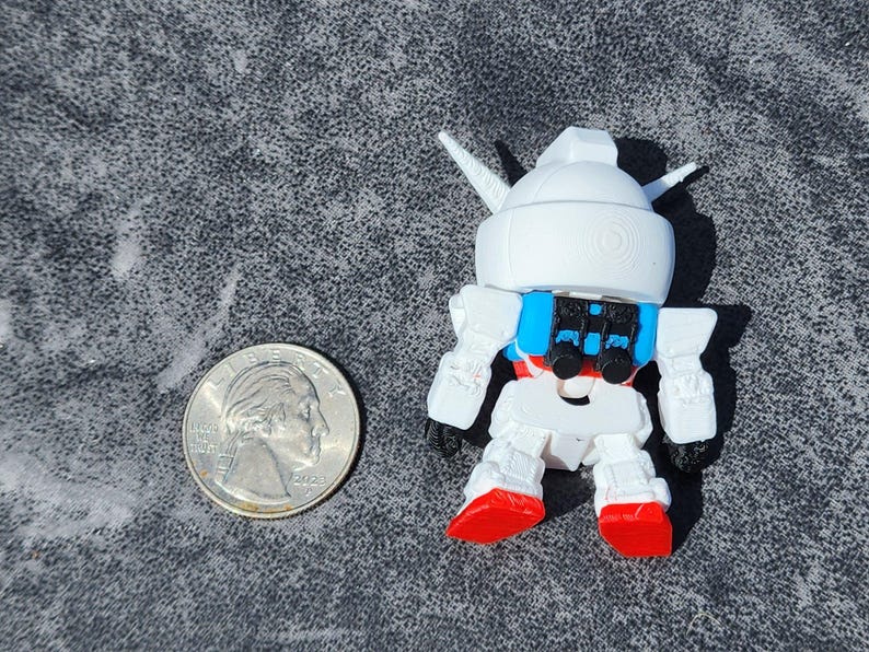May include: A small white robot figurine with a blue backpack and red feet, positioned next to a United States quarter coin for scale. The robot features a rounded head with two pointed antennae and articulated limbs, rendered in a stylized design.