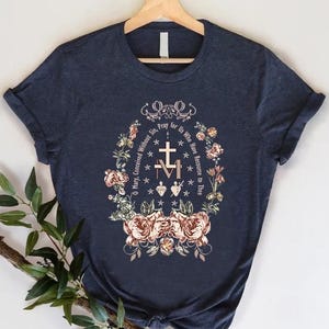 May include: A navy blue t-shirt with a floral design and the text "O Mary, Conceived Without Sin, Pray for Us Who Have Recourse to Thee."