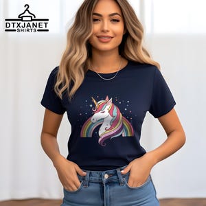 K&ouml;nnte beinhalten: Marineblaues T-Shirt mit einem bunten Einhorn-Design, Regenbogen und Sternen. Das Einhorn hat ein wei&szlig;es Gesicht, ein goldenes Horn und eine farbenfrohe M&auml;hne. Auf dem T-Shirt steht oben der Text "DTXJANET SHIRTS".