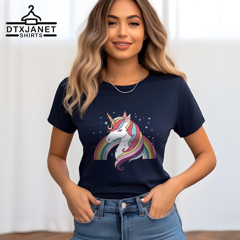 K&ouml;nnte beinhalten: Marineblaues T-Shirt mit einem bunten Einhorn-Design, Regenbogen und Sternen. Das Einhorn hat ein wei&szlig;es Gesicht, ein goldenes Horn und eine farbenfrohe M&auml;hne. Auf dem T-Shirt steht oben der Text "DTXJANET SHIRTS".