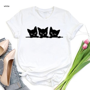 a white shirt with three black cats on it