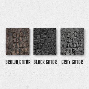 May include: Three square swatches featuring a textured alligator skin pattern in brown, black, and gray. Each swatch is labeled below with the text BROWN GATOR, BLACK GATOR, and GRAY GATOR, respectively, indicating the color of each sample.