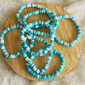 May include: A set of five turquoise and white beaded bracelets. The bracelets are made of small, round beads that are stacked on top of each other. The beads are a mix of turquoise and white, creating a striped pattern.