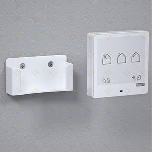 Op de afbeelding: Een witte wandmontage voor een bedieningspaneel en houder. Het bedieningspaneel heeft een touchscreen met huispictogrammen en de merknaam "VELUX". De houder is een eenvoudig, rechthoekig ontwerp met twee schroeven.