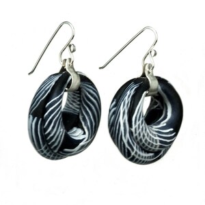 May include: A pair of black and white patterned earrings with silver hooks. The earrings are made of polymer clay and have a unique, twisted design.