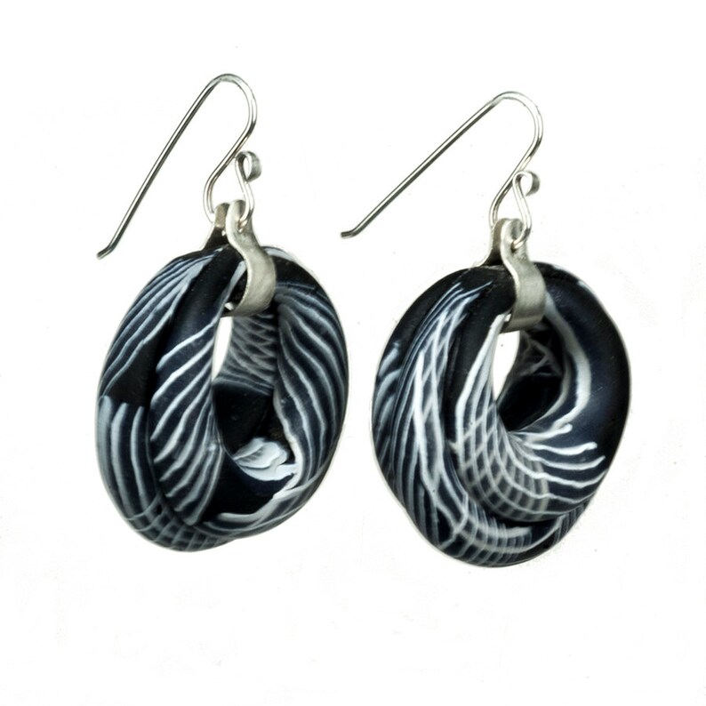 May include: A pair of black and white patterned earrings with silver hooks. The earrings are made of polymer clay and have a unique, twisted design.