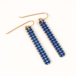 May include: A pair of blue and white enamel earrings with a gold hook. The earrings are rectangular and have a dotted pattern.