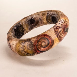 May include: A brown bangle bracelet with a decorative pattern of seashells and swirls in shades of brown, red, and white.