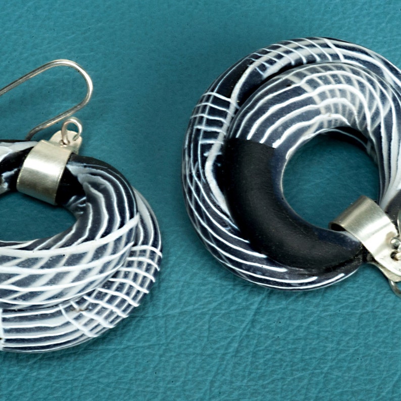 May include: A pair of black and white ceramic earrings with silver hooks. The earrings are made of twisted clay with a geometric pattern.