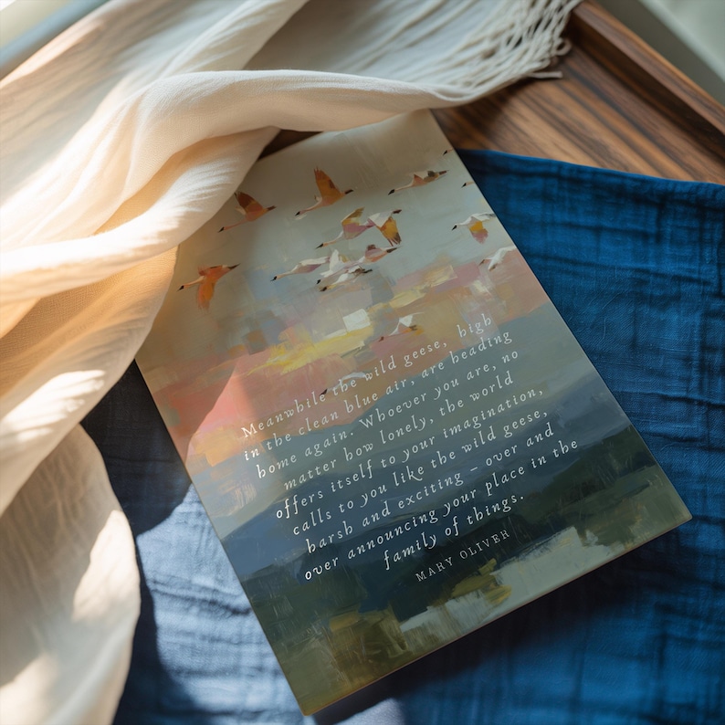 May include: A rectangular art print with a watercolour painting of geese in flight against a sunset sky. The print includes a quote by Mary Oliver. The print rests on a blue cloth, with cream-coloured fabric draped nearby.