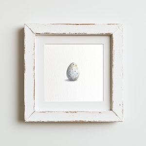 May include: A watercolor painting of a speckled bird egg in a white frame. The egg is light blue with dark blue and gold speckles.