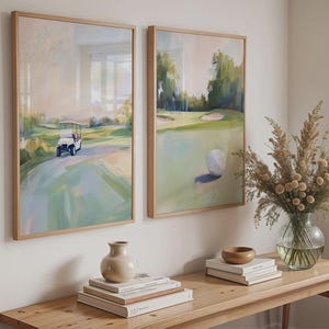 May include: Two framed abstract paintings depicting a golf course. The painting on the left shows a golf buggy driving on the course. The painting on the right shows a golf ball on the green. The paintings are hanging on a white wall above a wooden table with books and a vase of dried flowers.