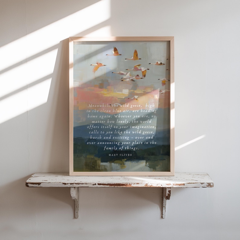 May include: A framed art print with a painting of geese flying in a colorful sky. The artwork includes a quote by Mary Oliver. The frame is light-colored, and the print is displayed on a white shelf, adding a touch of elegance.
