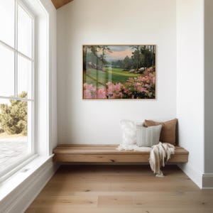 Puede incluir: Pintura enmarcada de un paisaje de campo de golf con flores rosas en primer plano. El cuadro cuelga sobre un banco de madera con cojines y una manta. La habitaci&oacute;n tiene una ventana grande y suelo de madera clara.