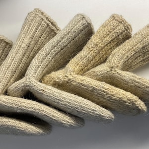 May include: A collection of beige knitted gloves, arranged in a fan shape. The gloves have a ribbed texture and a curved design at the wrist. The color is a natural, off-white hue.